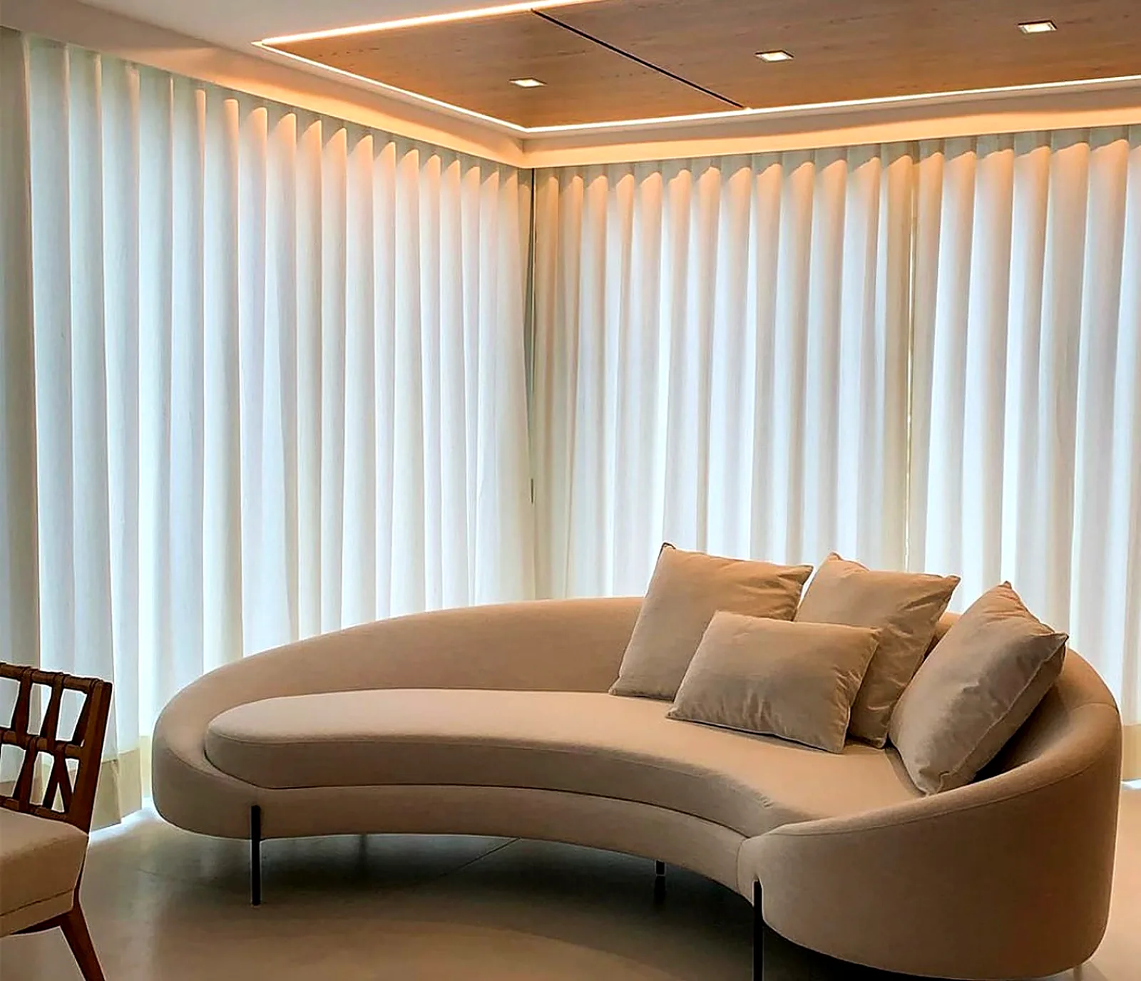 Cortina de tecido leve com caimento em ondas em sala com sofá curvo e sanca iluminada