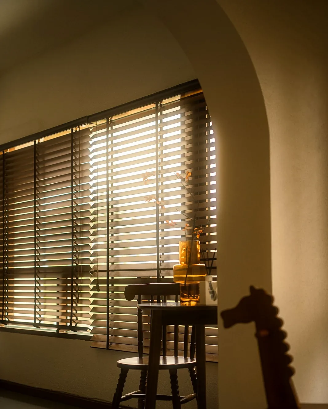 Persiana horizontal de madeira em sala com arco e cadeira de madeira sob luz natural